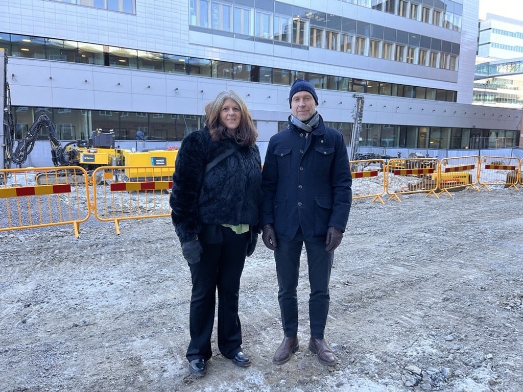 En man och en kvinna står framför en byggnad vid en byggarbetsplats.