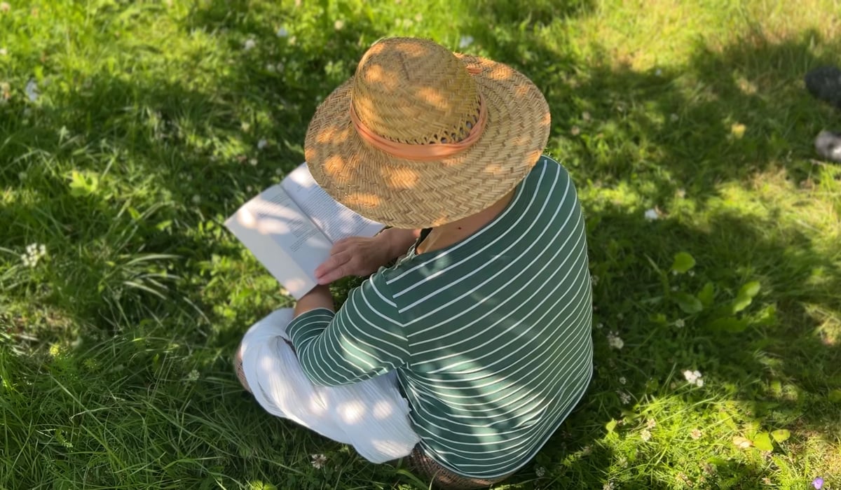 Kvinna sitter i skugga med täckande kläder och hatt